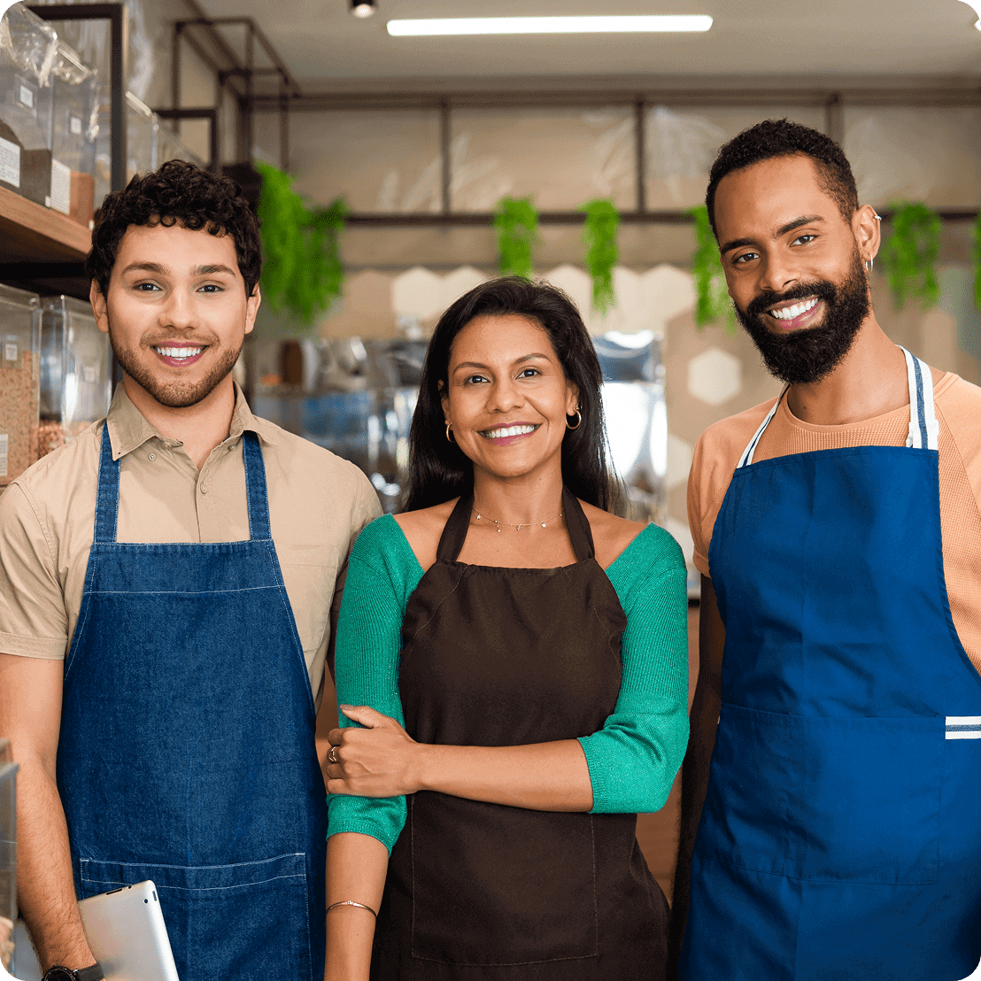 Three smiling people wearing aprons in store.