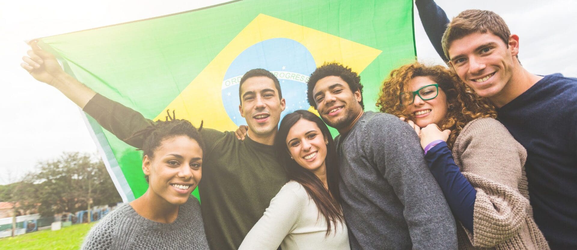 A group of four friends smiling with a Brazilian flag in the background.