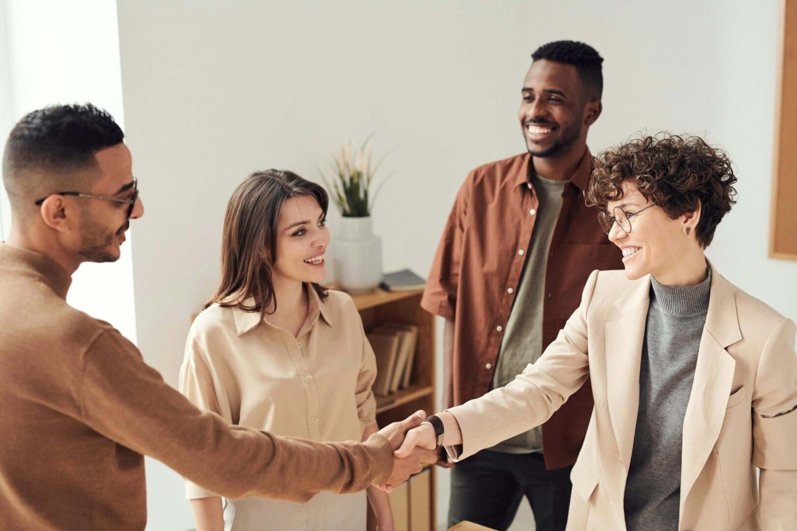 Four colleagues shaking hands and smiling in a bright office.