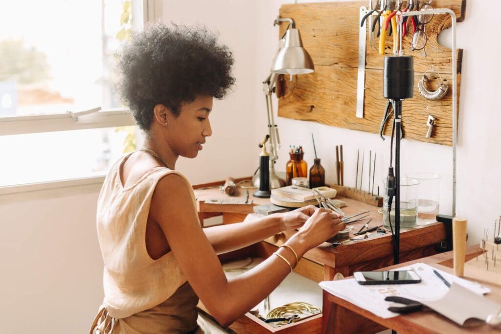 Woman crafting jewelry at a wooden workbench in a bright studio.