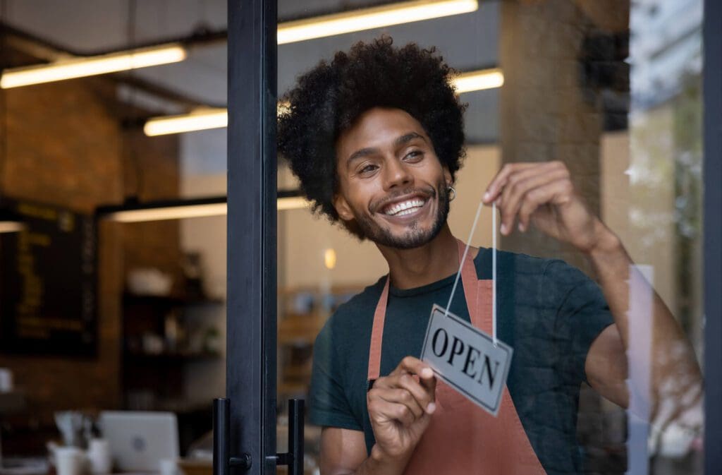 Smiling barista hanging an open sign on a café door.
