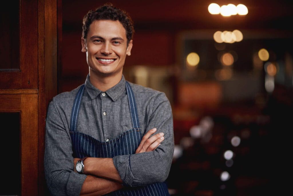 Smiling young man with crossed arms in a cozy restaurant setting.