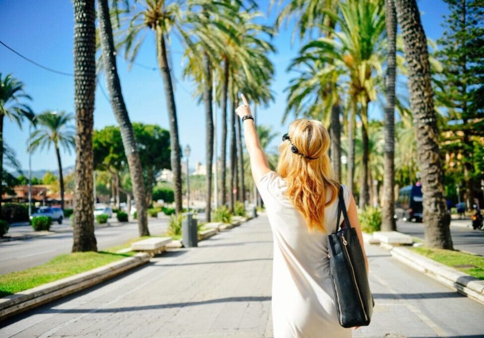 Woman walking along a palm tree avenue.
